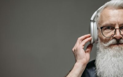 Gros plan d'un homme âgé avec une barbe et des lunettes, écoutant de la musique avec des écouteurs.