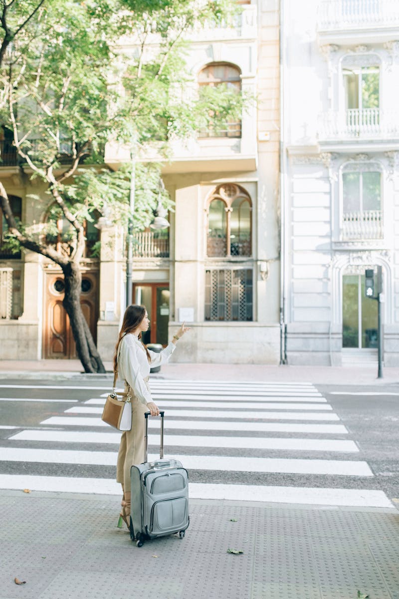 Une jeune femme avec une valise se tient sur un passage piéton de la ville, pointant vers l'avant.